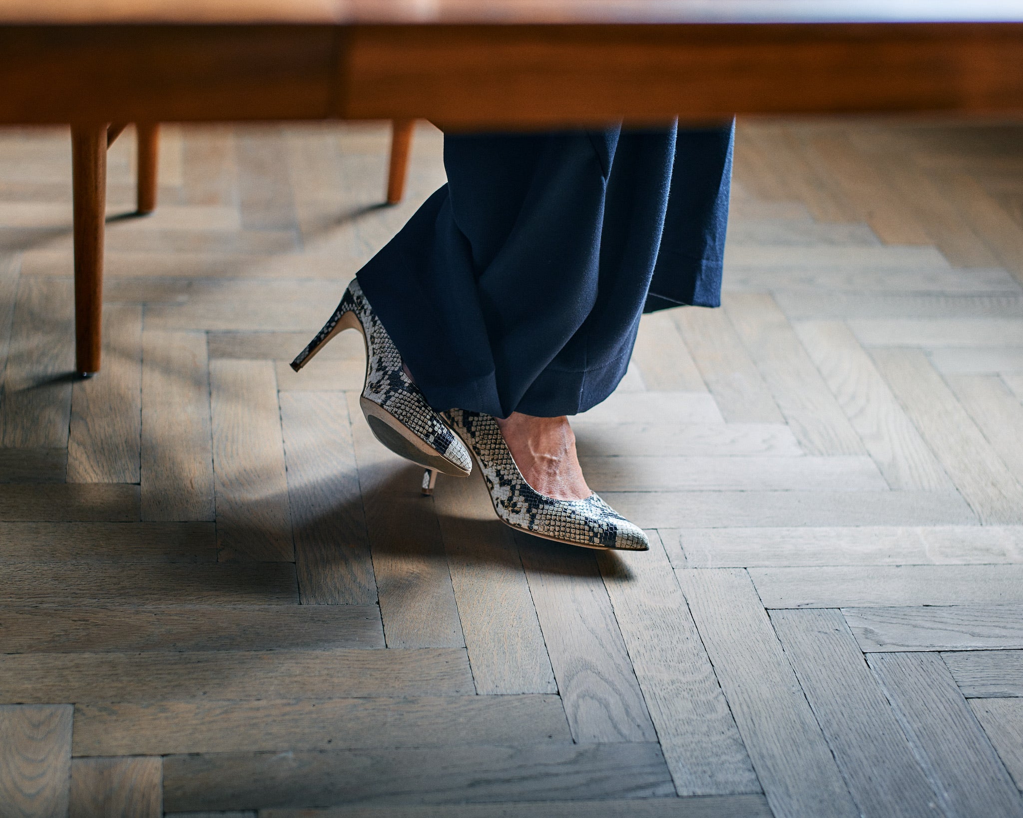 legs of a woman wearing python high heels under a desk