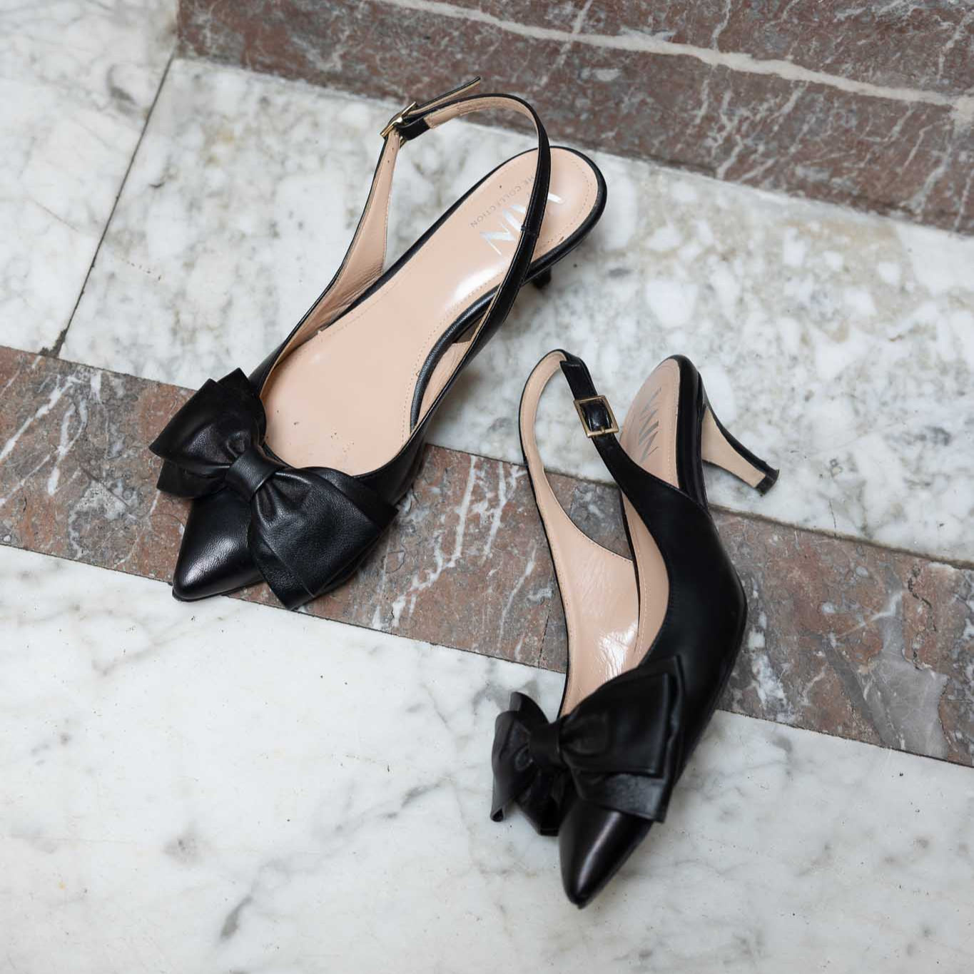 Black low-heeled slingback shoes with bow details on a marble floor