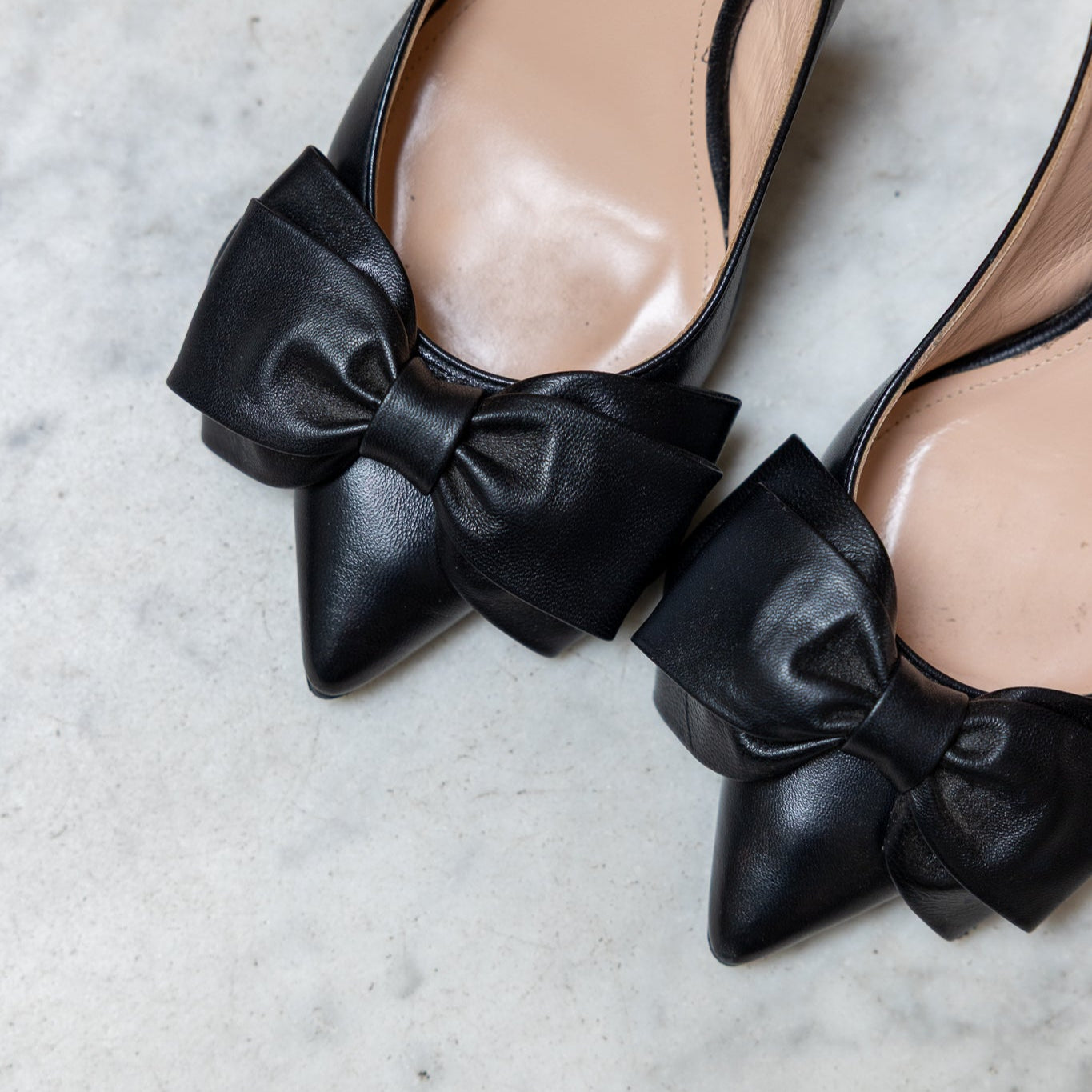 Black pointed-toe slingback shoes with bow details on a light gray surface