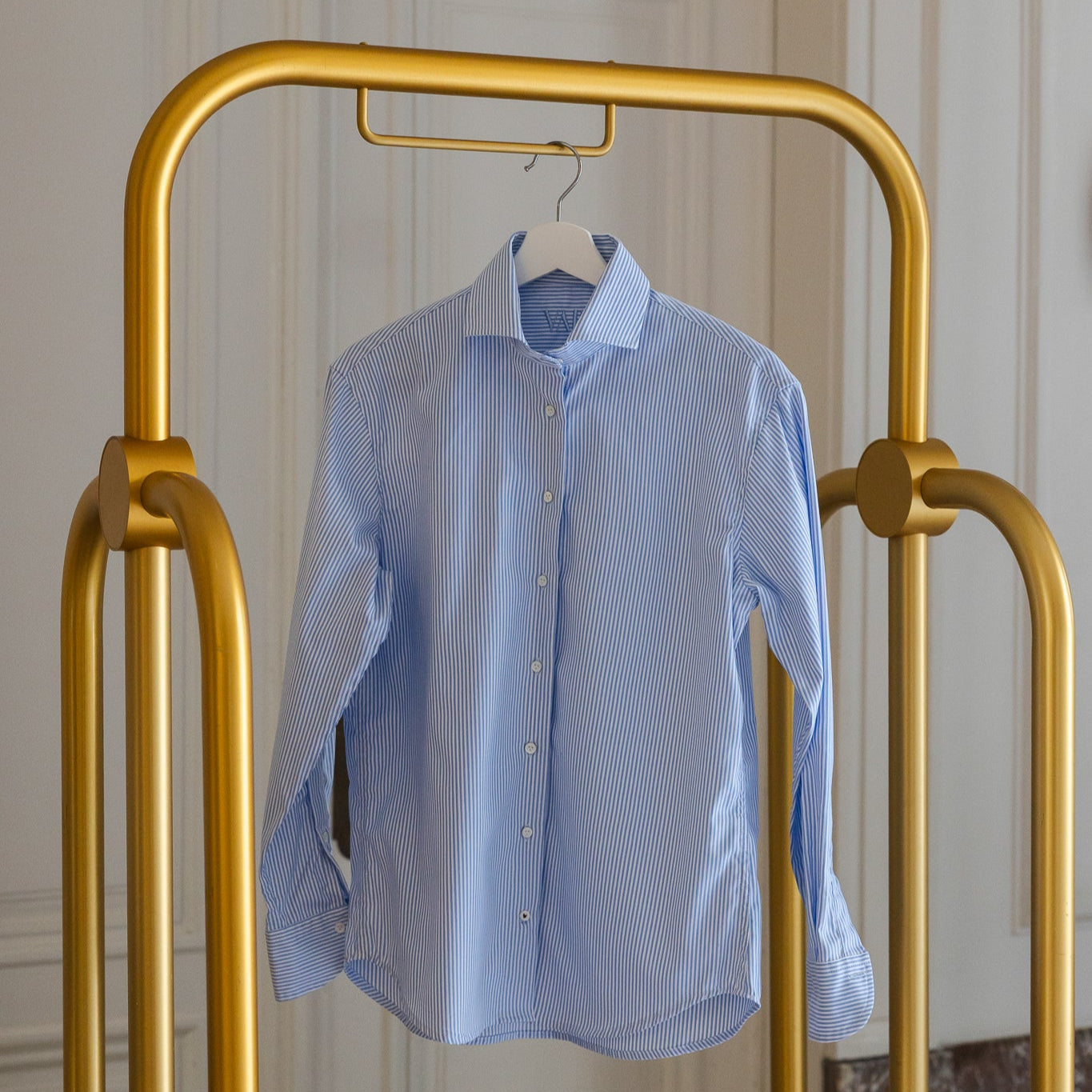 Blue White striped shirt on a gold garment rack against a neutral wall.