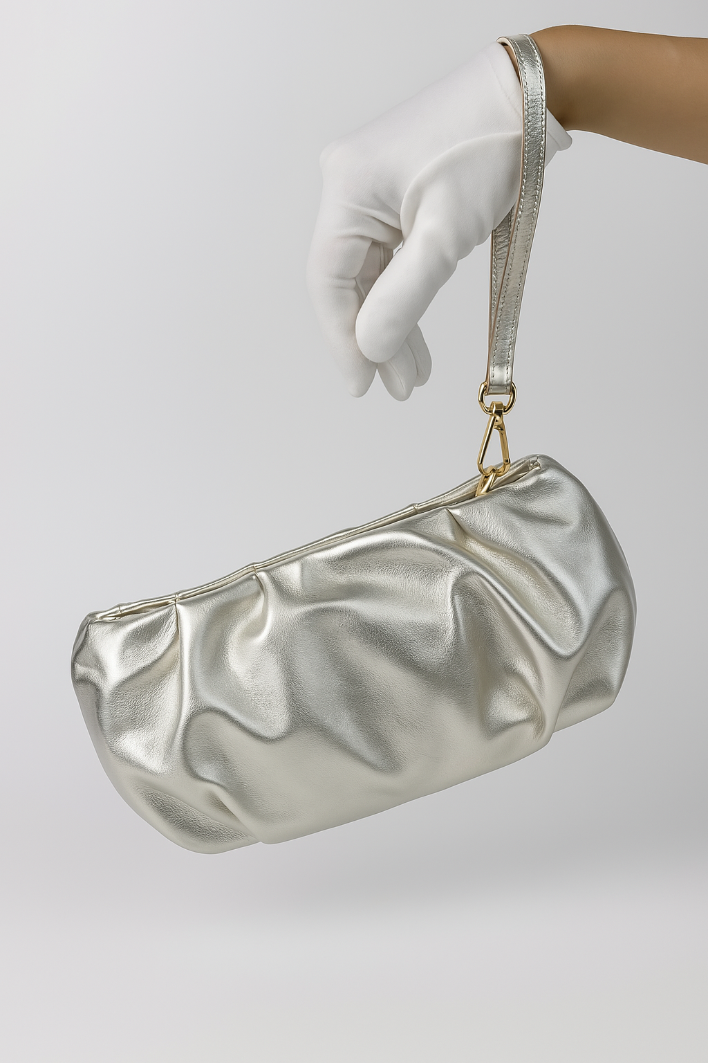 Champagne clutch with wrist strap held by a gloved hand against a light background