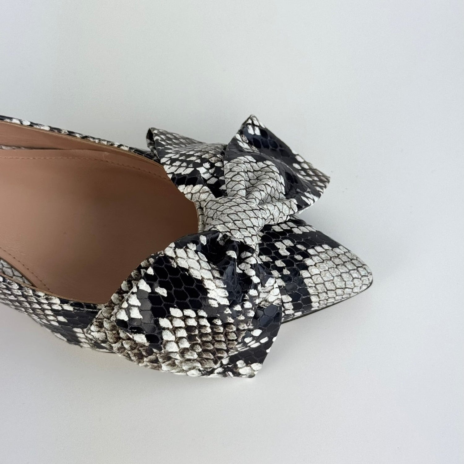 Detail of Faux Python sling back kitten heel with a bow on a white background