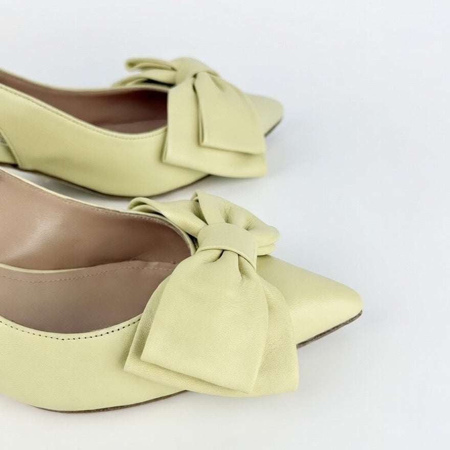 Detail of pair of yellow los-heeled sling back shoes with large bows on a white background