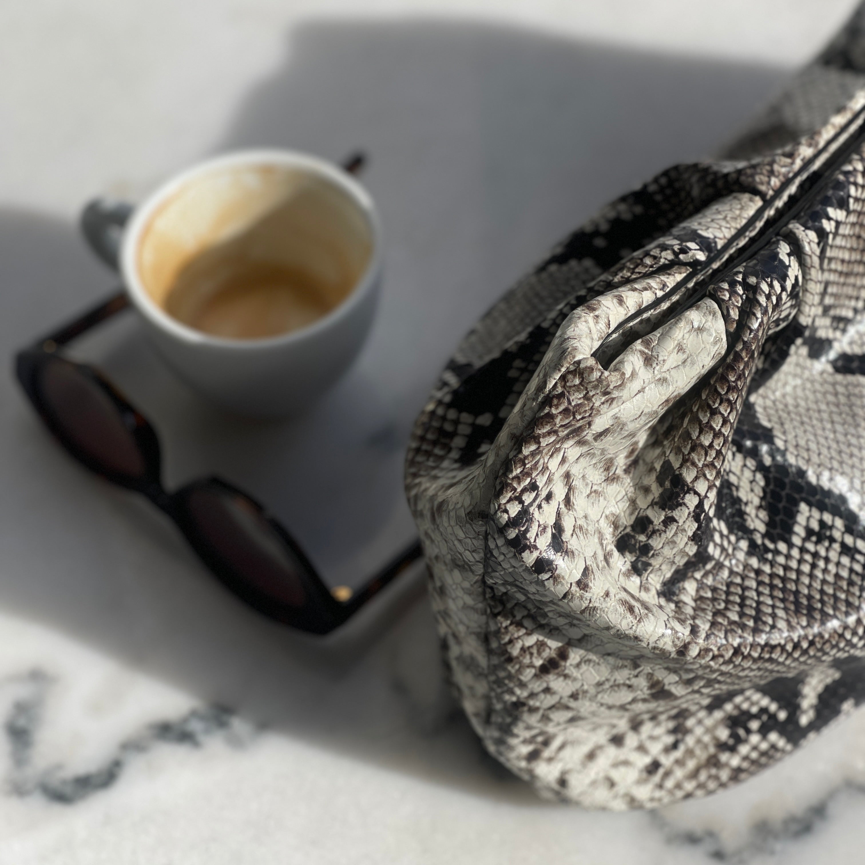 Faux Python large clutch next to a cup of coffee and sunglasses on a marble surface