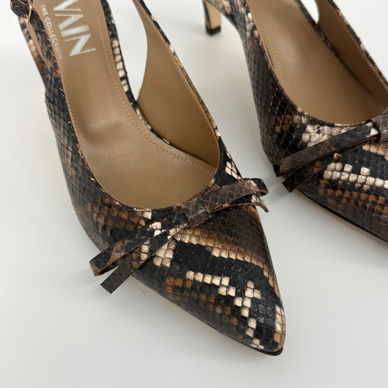 A pair of pointed-toe slingback pumps with a brown, black, and beige snakeskin pattern, featuring a small bow detail on the toe and the brand name &
