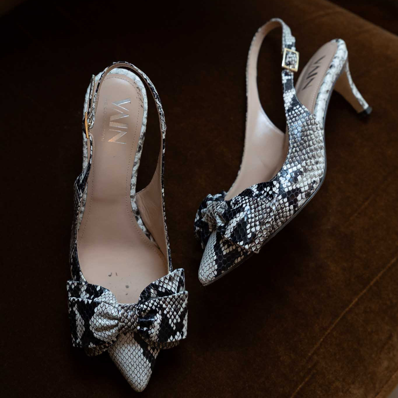 Pair of low-heeled sling back heels with decorative bows on a brown velvet chair