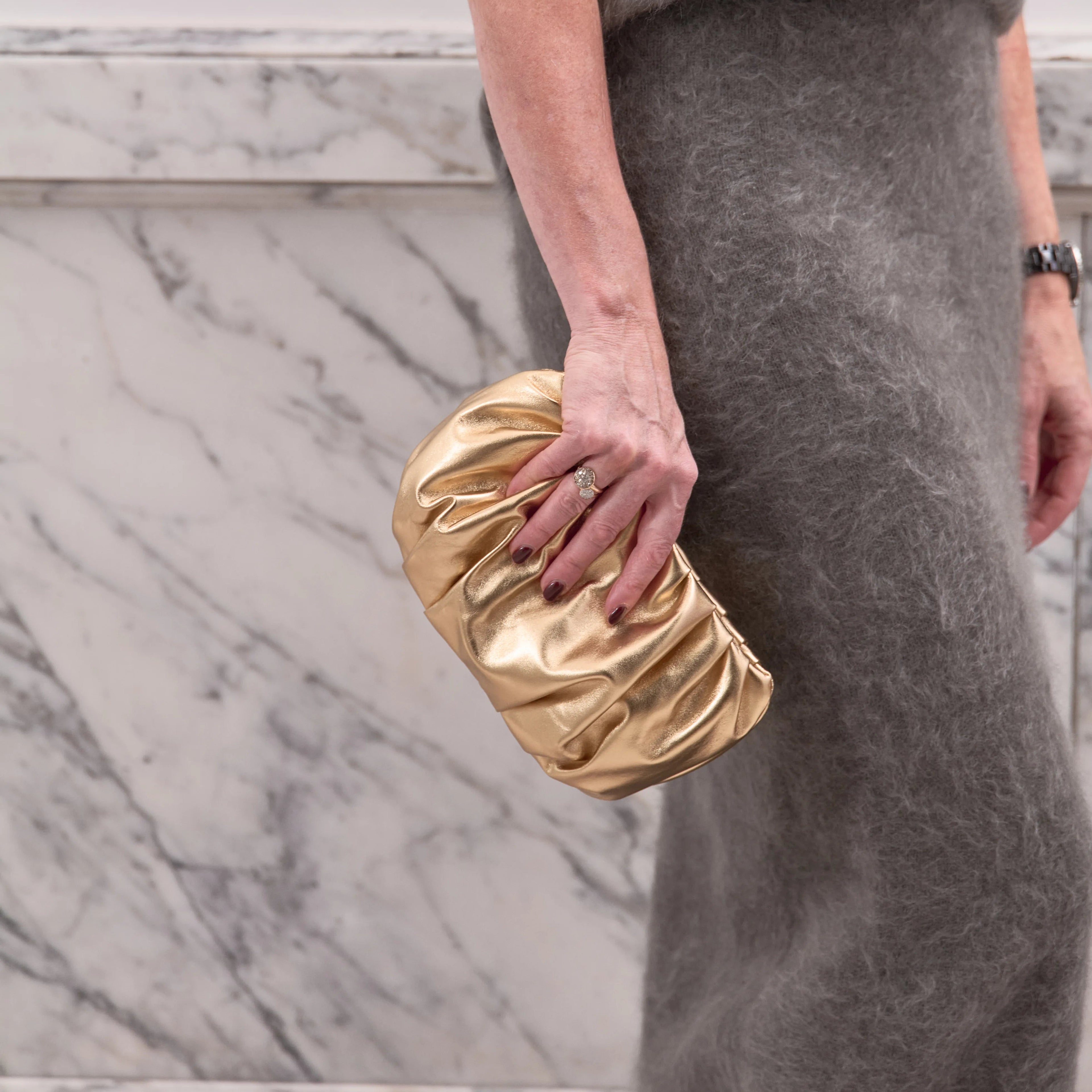 Person holding a gold clutch against a marble wall