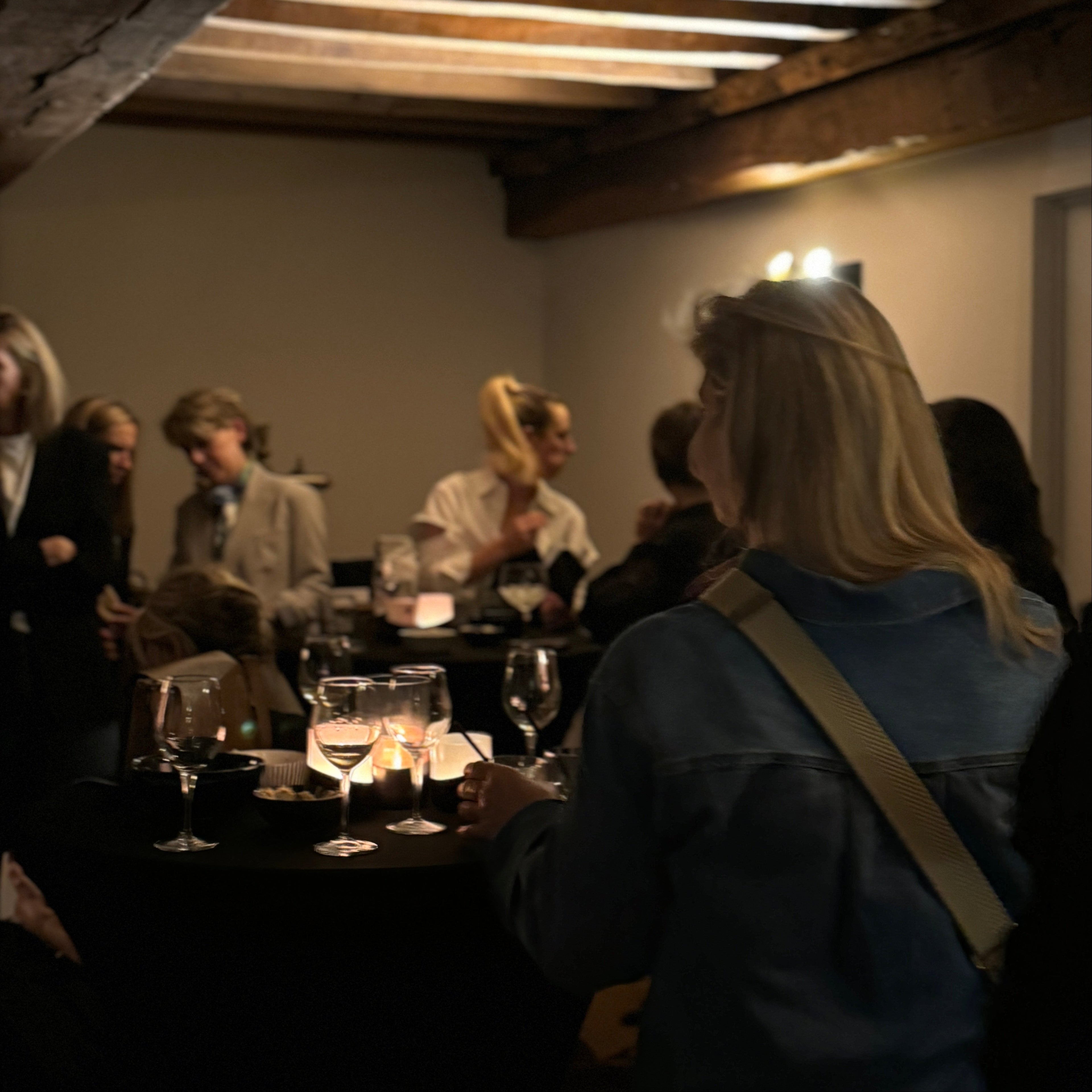 People sitting at a table with drinks in a dimly lit room with wooden beams.