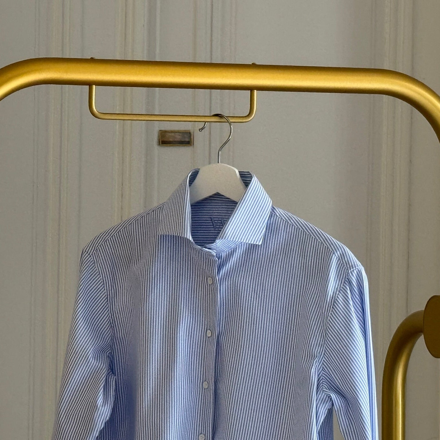 blue white striped blouse with stiff collar hanging at a rack in front of white classy door
