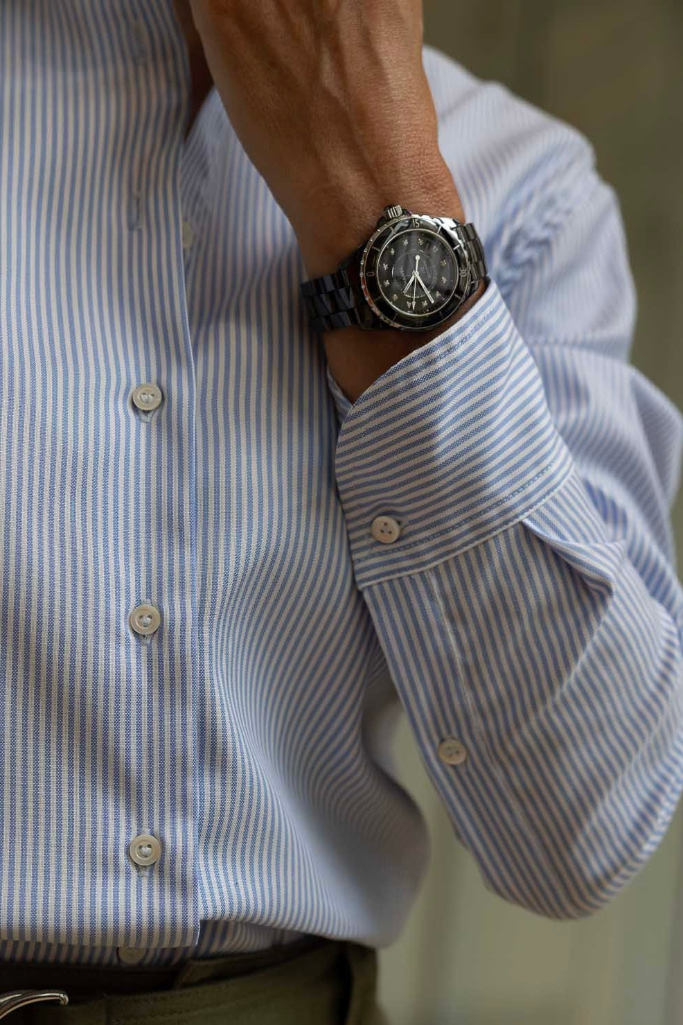 Close-up of a wrist wearing a watch with a blue striped shirt.