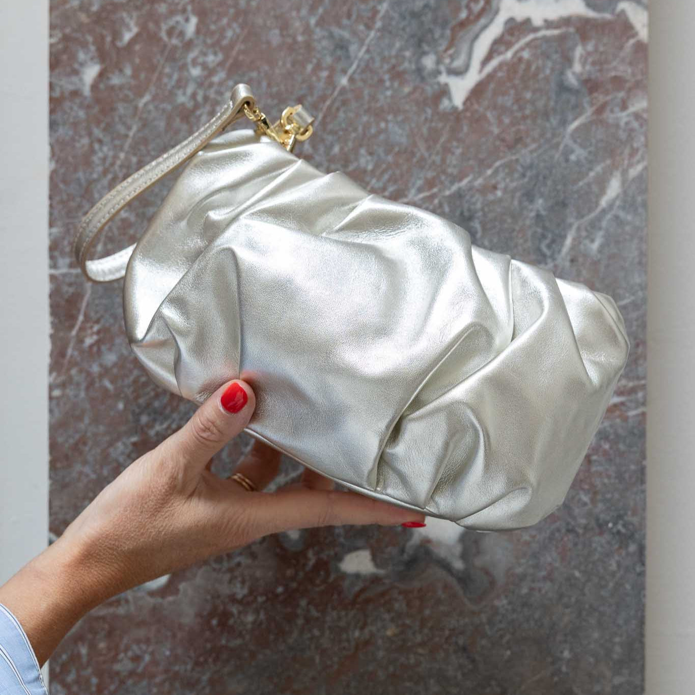 Hand holding a champagne coloured leather clutch bag against a marble background