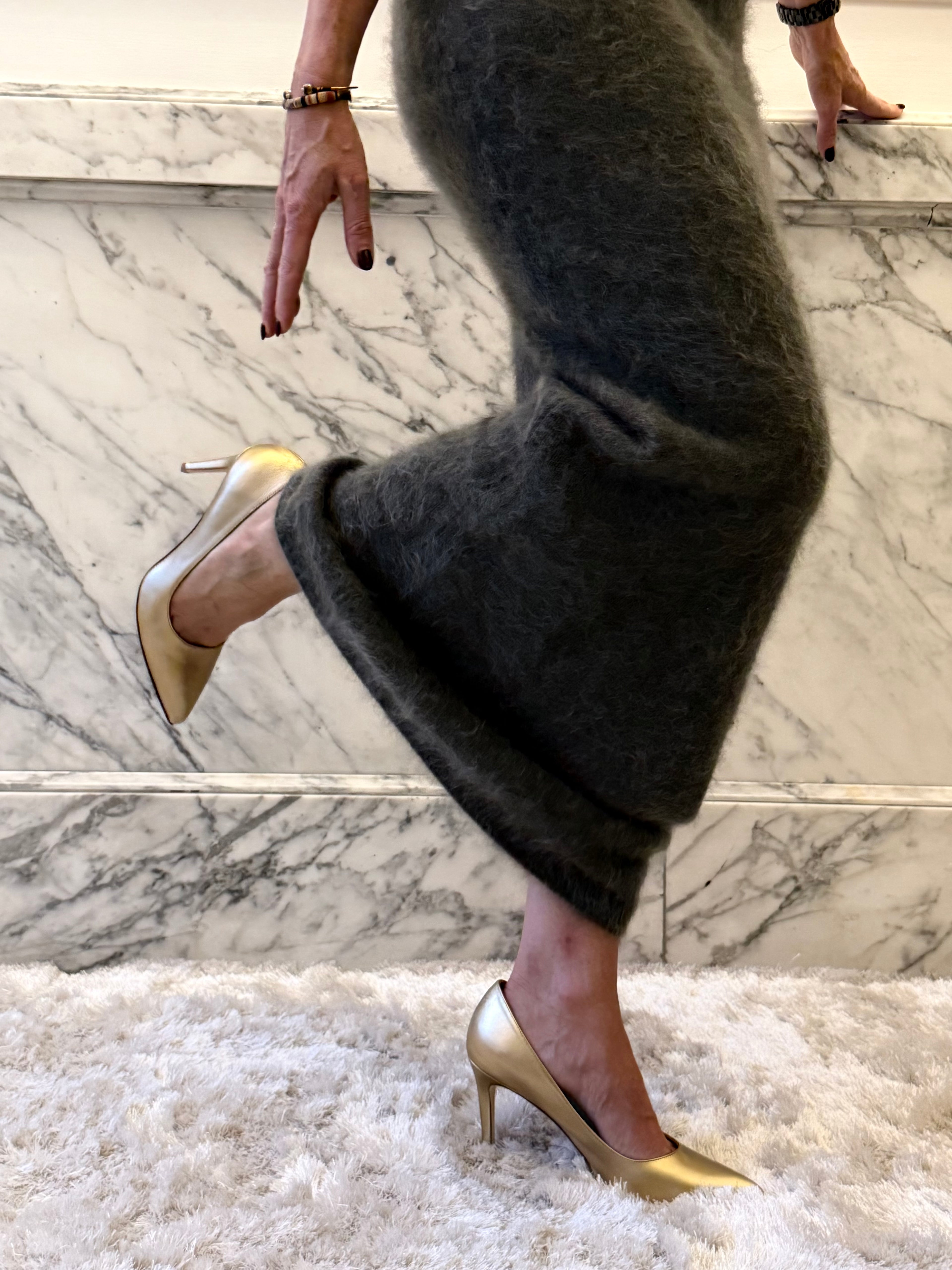 Person wearing gold high heels and dark green long skirt on a marble staircase.