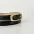 A close-up of a black leather belt with a polished gold-tone metal buckle, showing the inner tan lining, set against a plain light gray background.