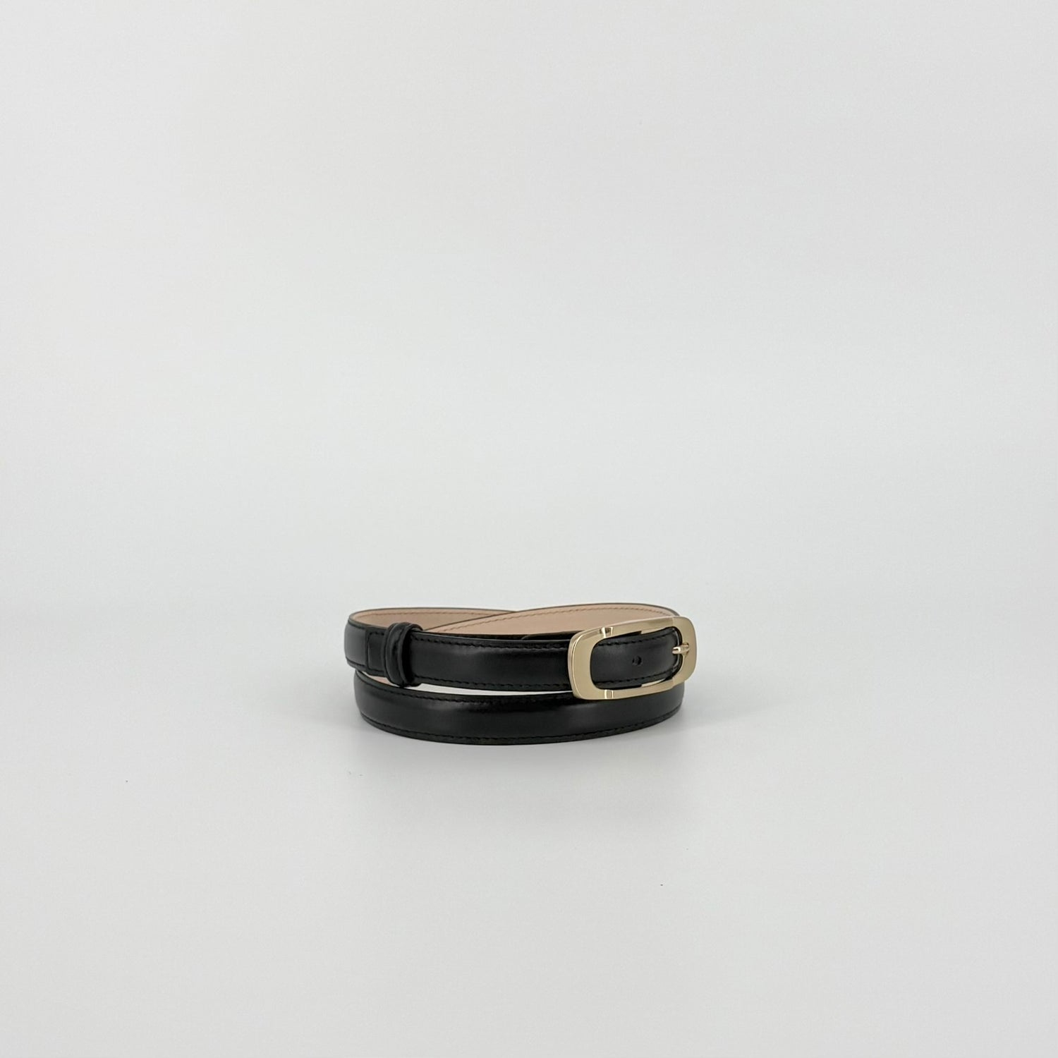 Black leather belt with a polished gold-tone metal buckle, showing the inner tan lining, set against a plain light gray background.