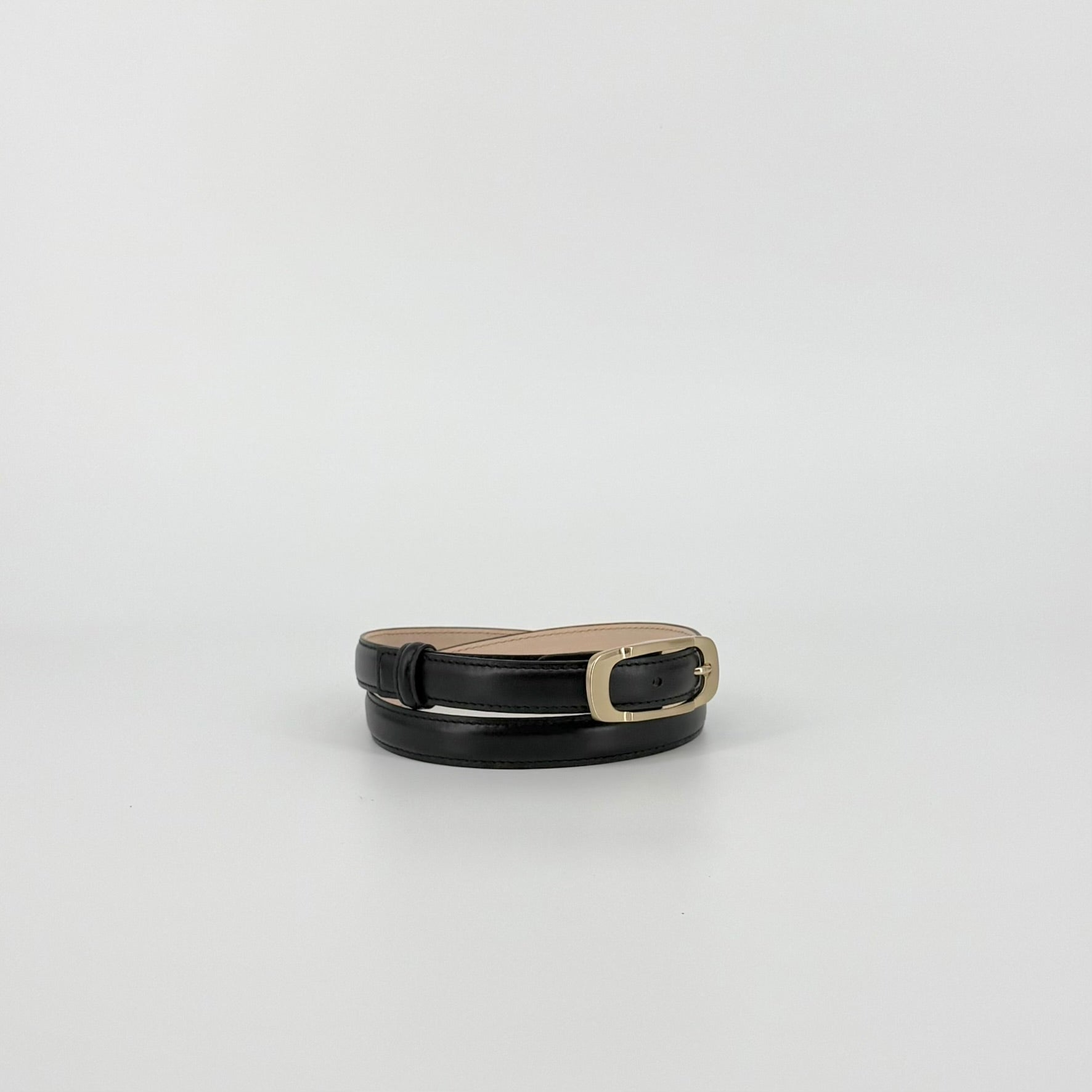 Black leather belt with a polished gold-tone metal buckle, showing the inner tan lining, set against a plain light gray background.
