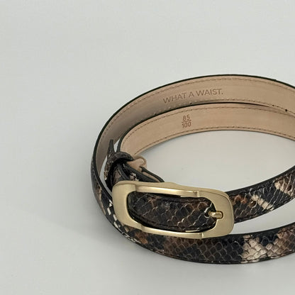 A brown and black snakeskin-patterned leather belt with a gold-tone buckle, displayed on a light gray background. The inside of the belt shows the text &