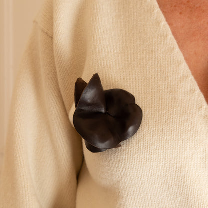 A close-up of a person wearing a cream-colored knit cardigan with a dark brown leather flower-shaped brooch pinned to the chest.