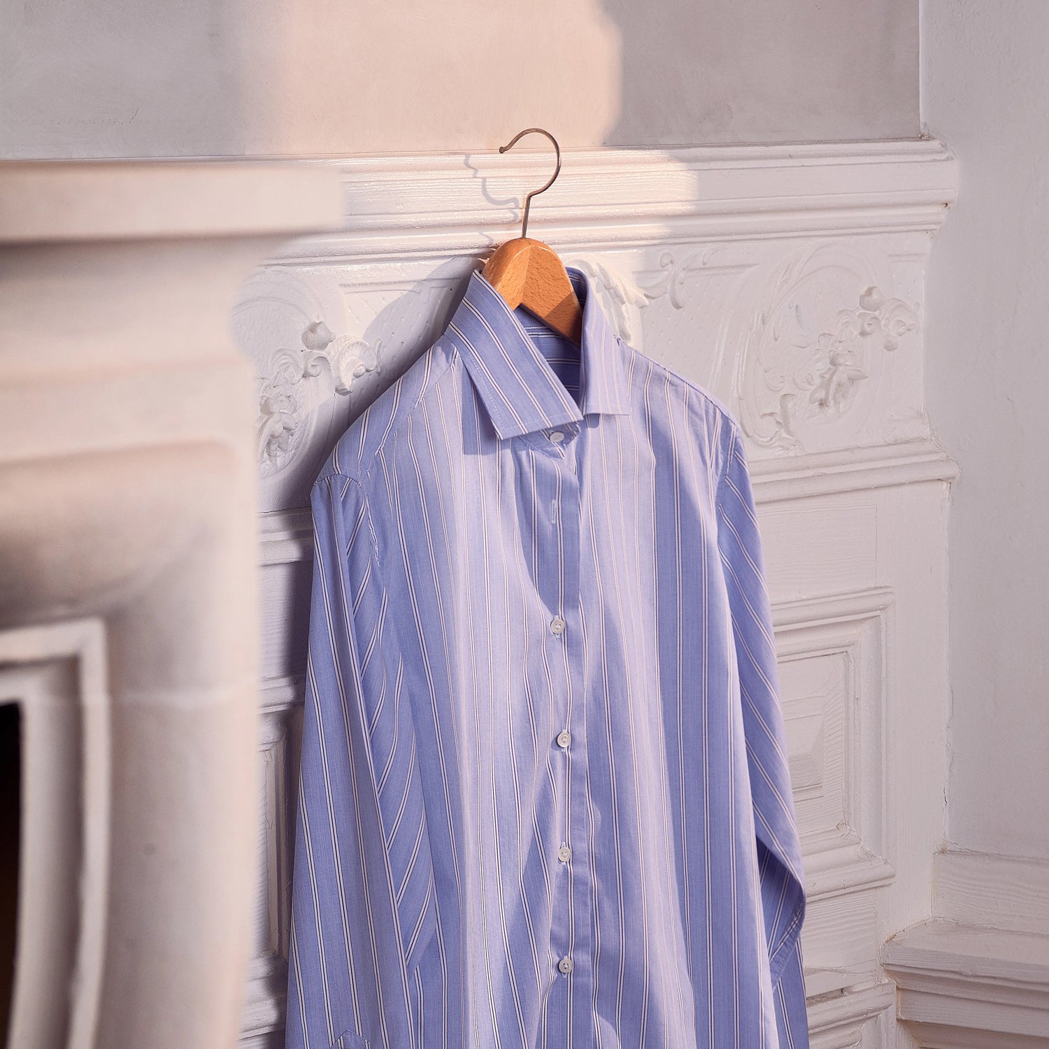 Blue striped shirt hanging on a hook against a decorative wall.