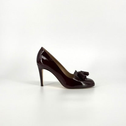 One dark burgundy patent leather pump with tassel details on the toes, shown from the side against a plain white background.