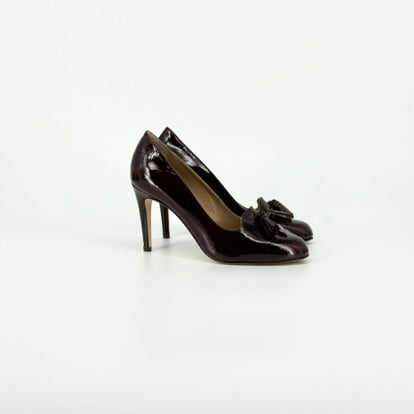 A pair of dark burgundy patent leather pumps with tassel details on the toes, shown from the side against a plain white background.