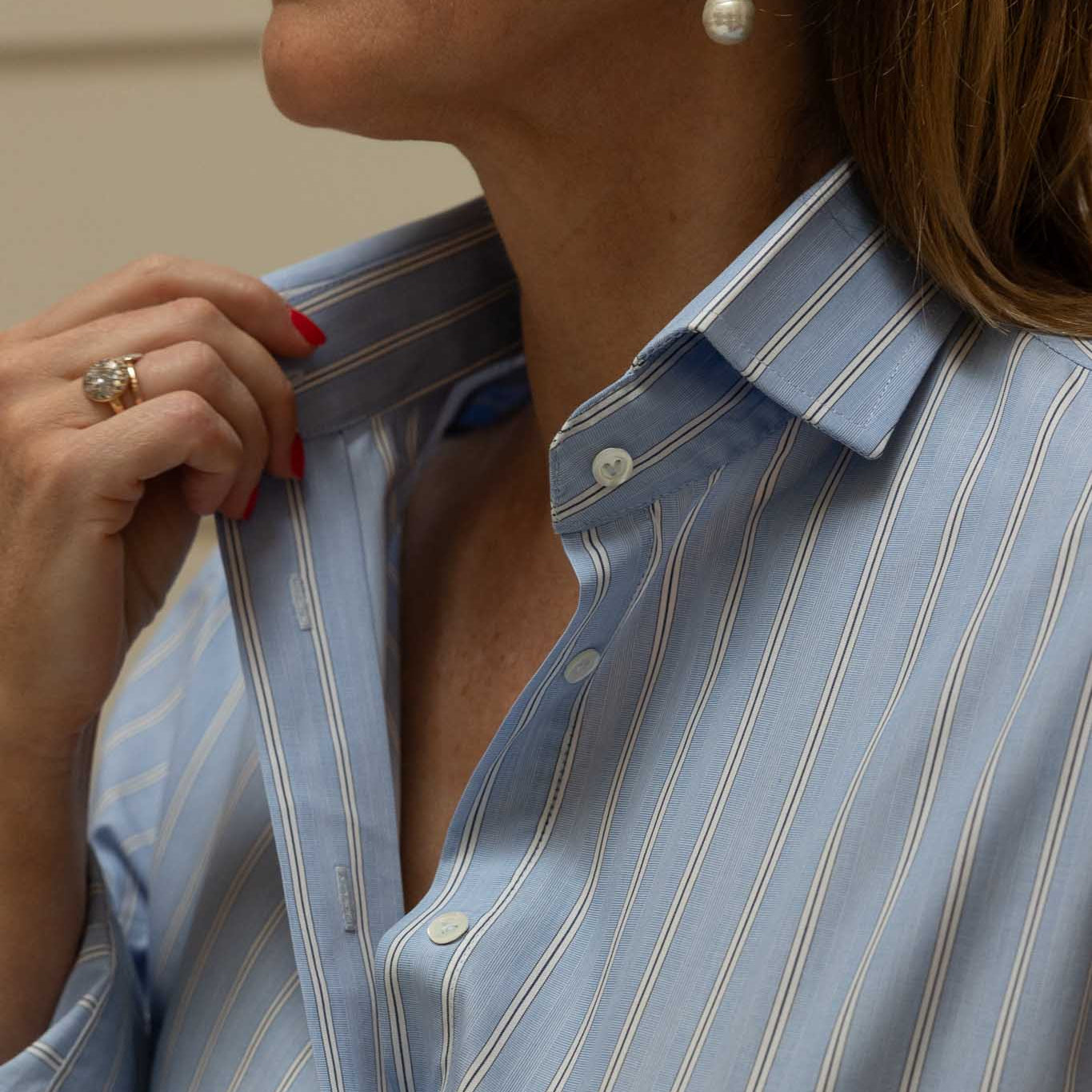 Close-up of a woman wearing a light blue striped shirt with pearl earrings.