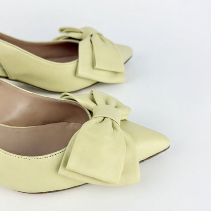 Detail of pair of yellow los-heeled sling back shoes with large bows on a white background