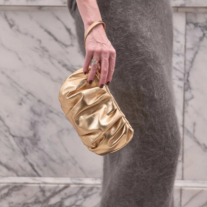 Gold clutch held by a person wearing a gray outfit against a marble wall.