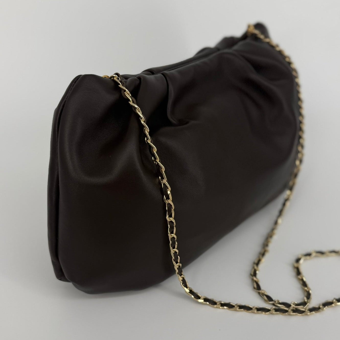 Large soft nappa leather clutch in dark brown with metallic strap on a white background