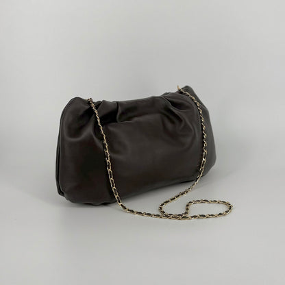A dark brown leather shoulder bag with a gold chain strap, photographed on a neutral light gray background.