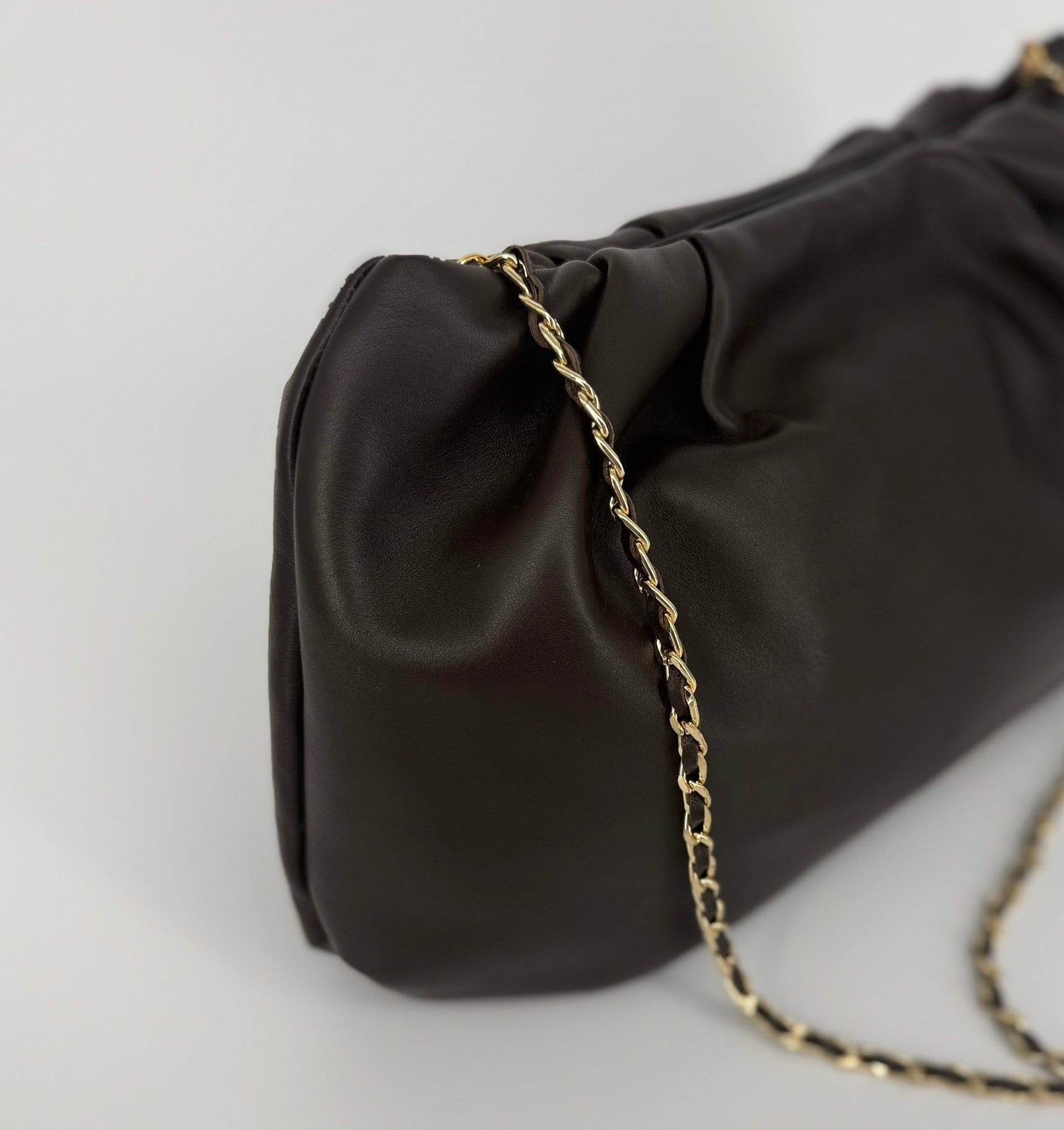A close-up of a dark brown leather shoulder bag with a gold chain strap, set against a clean light gray background.