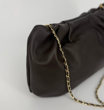 A close-up of a dark brown leather shoulder bag with a gold chain strap, set against a clean light gray background.