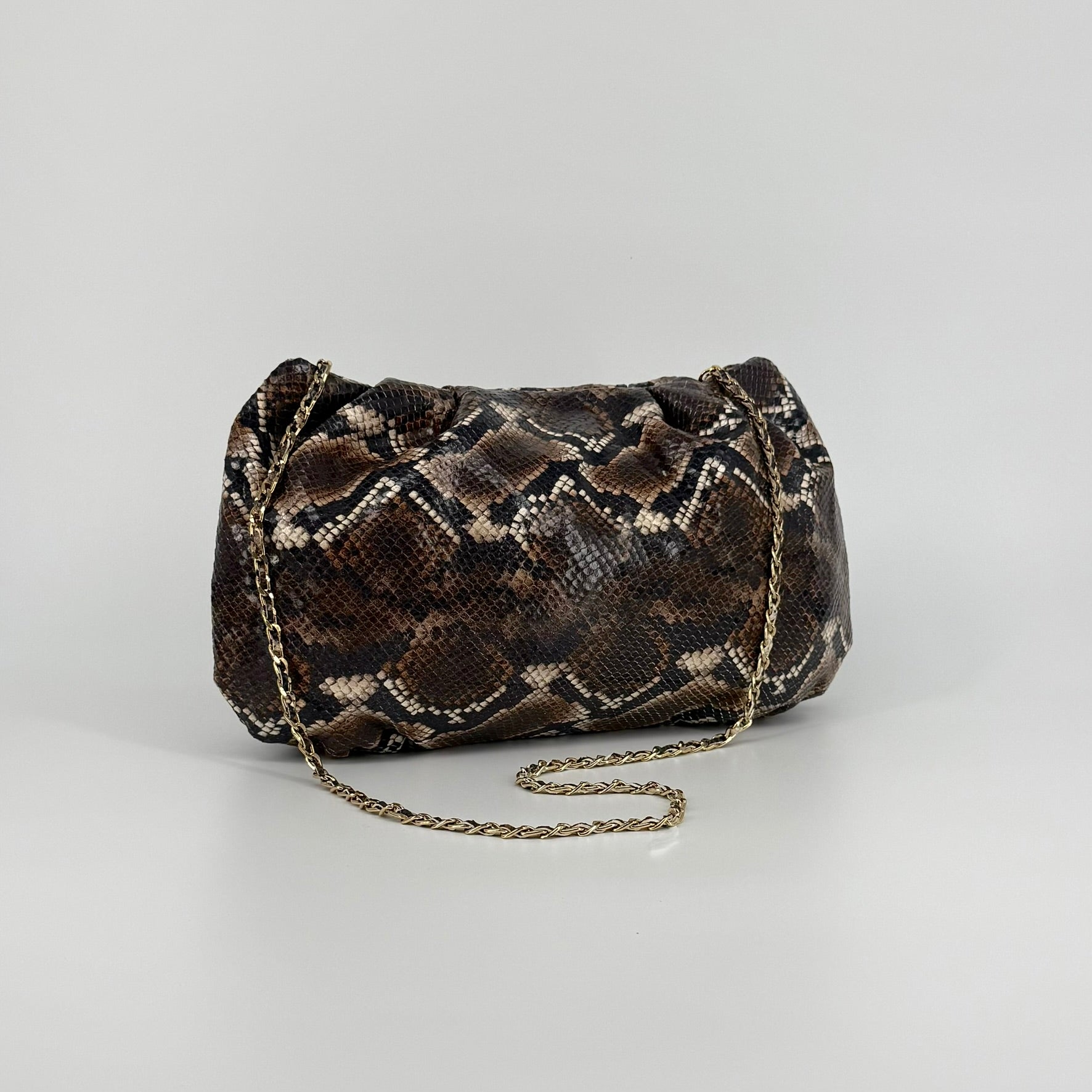 large clutch bag in a feminine folded shape in brown and black python printed leather with metallic strap on a white background