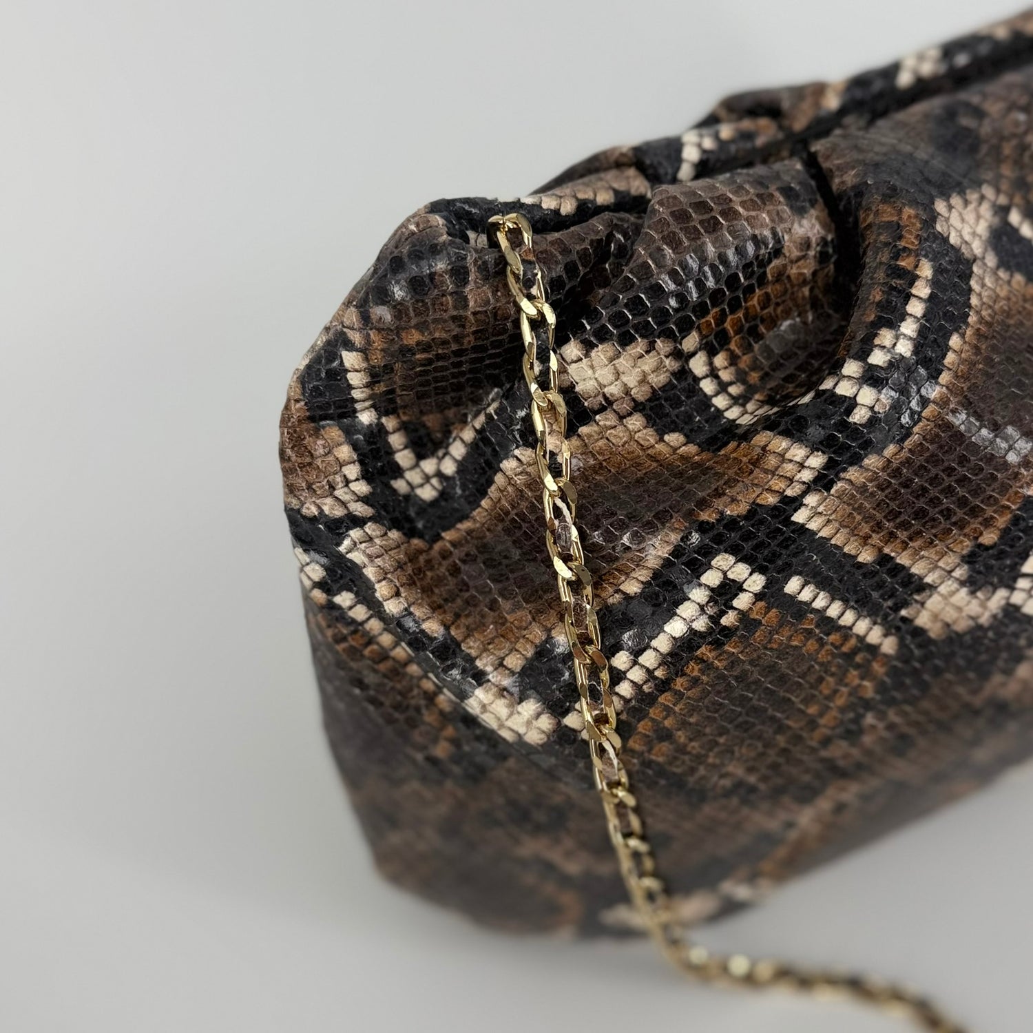 detail of large clutch bag in a feminine folded shape in brown and black python printed leather on a white background