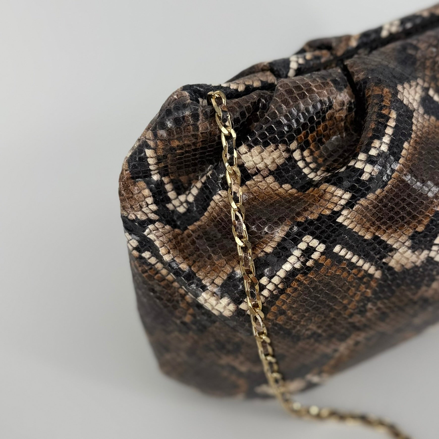 detail of large clutch bag in a feminine folded shape in brown and black python printed leather on a white background