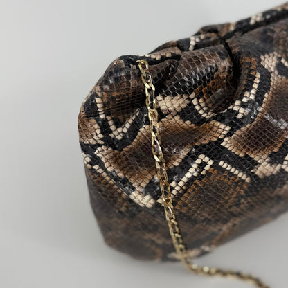 detail of large clutch bag in a feminine folded shape in brown and black python printed leather on a white background
