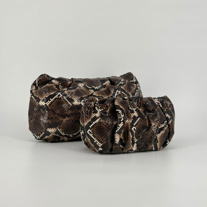 Mini and maxi snakeskin-patterned clutch bags in brown, black, and beige tones, photographed on a clean light gray studio background.
