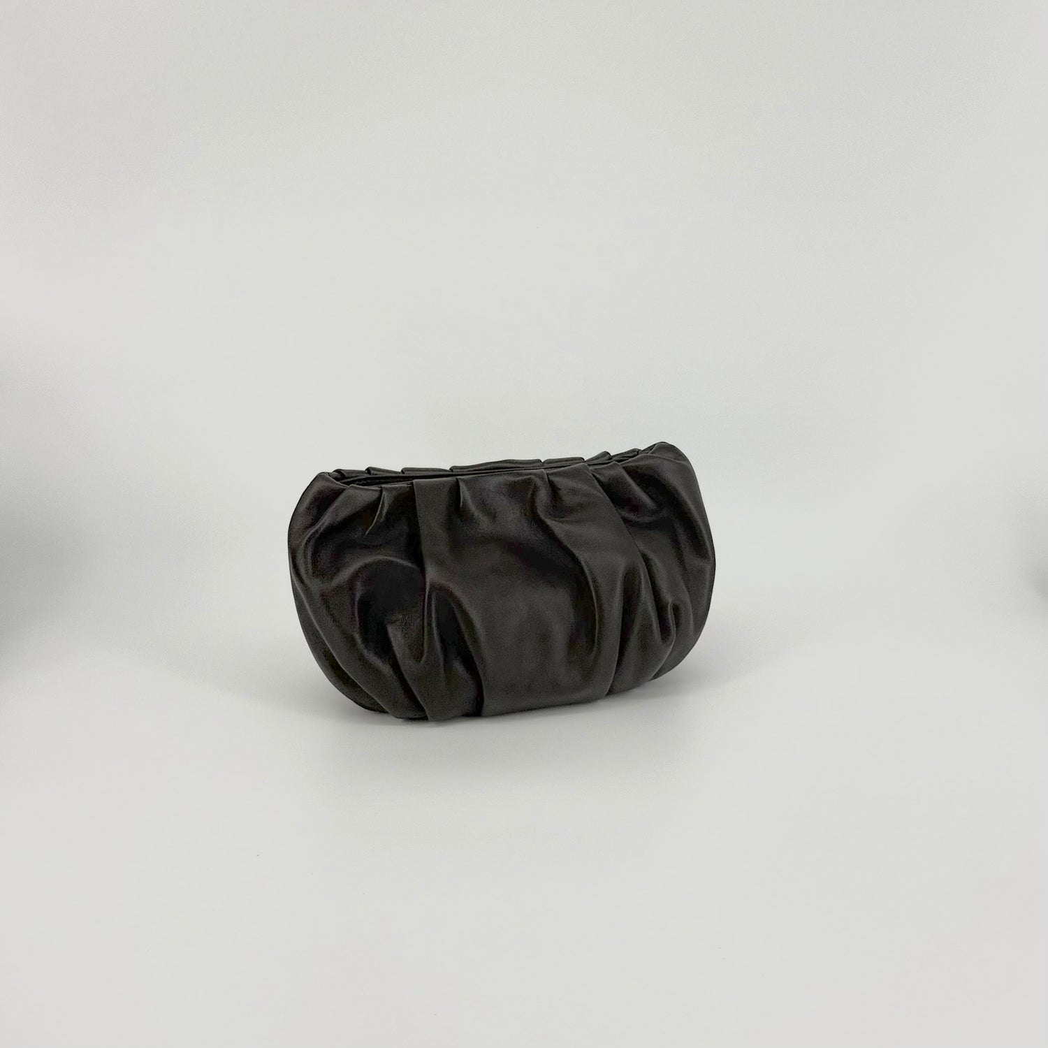 A dark brown leather clutch bag with a gathered, pleated design, photographed on a neutral light gray studio background.
