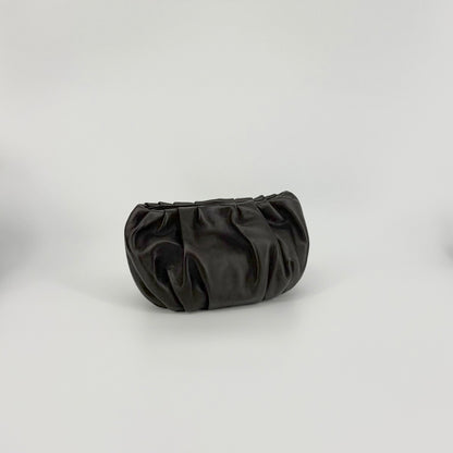 A dark brown leather clutch bag with a gathered, pleated design, photographed on a neutral light gray studio background.