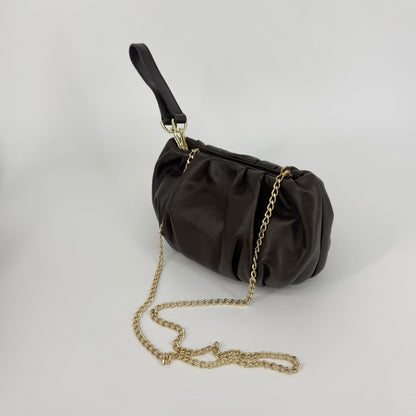 A dark brown pleated nappa leather clutch handbag with a gold chain strap and a dark brown wristlet strap, displayed on a light gray background.