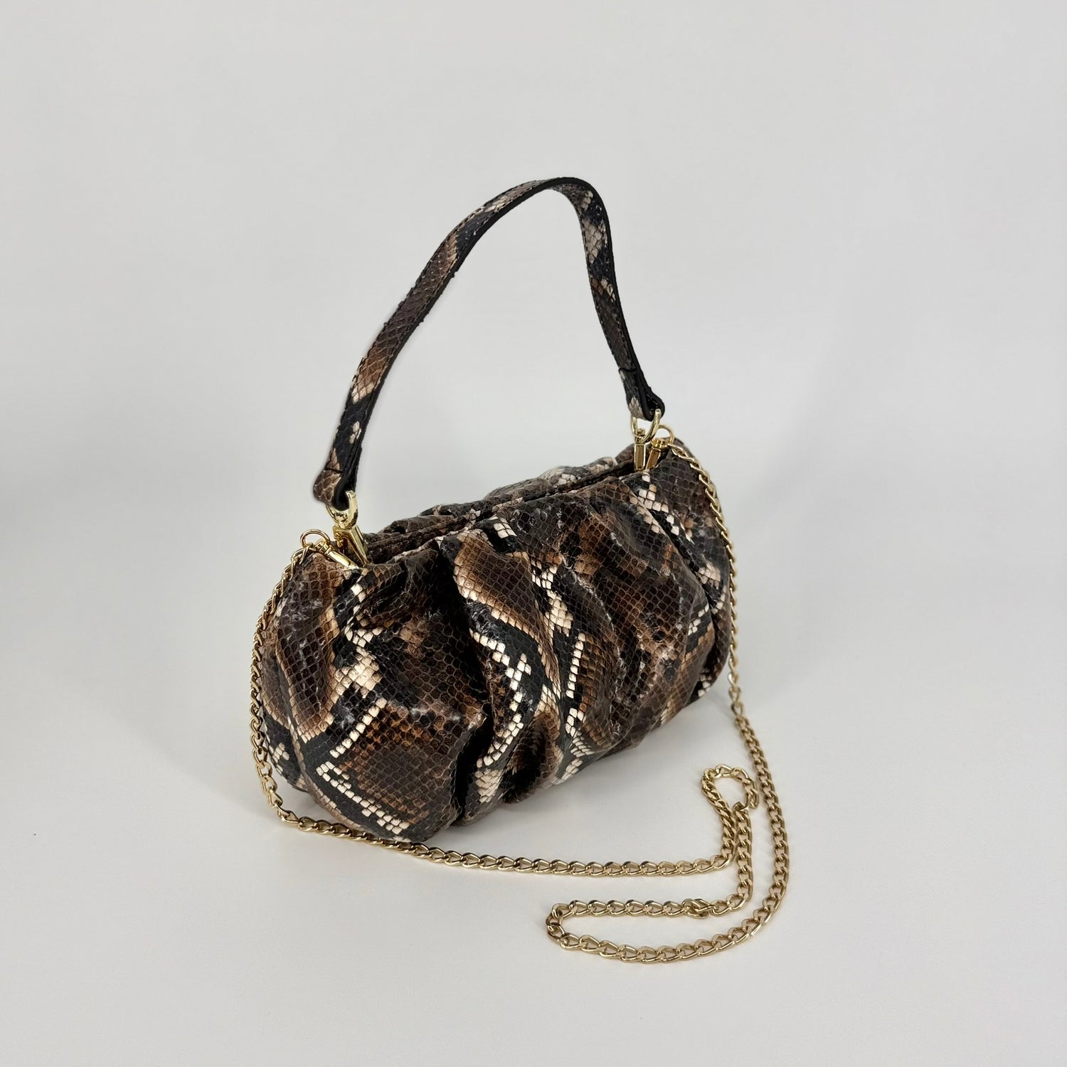 A snakeskin-patterned clutch bag with a gold-tone chain strap, and wrist strap displayed on a neutral light gray background.