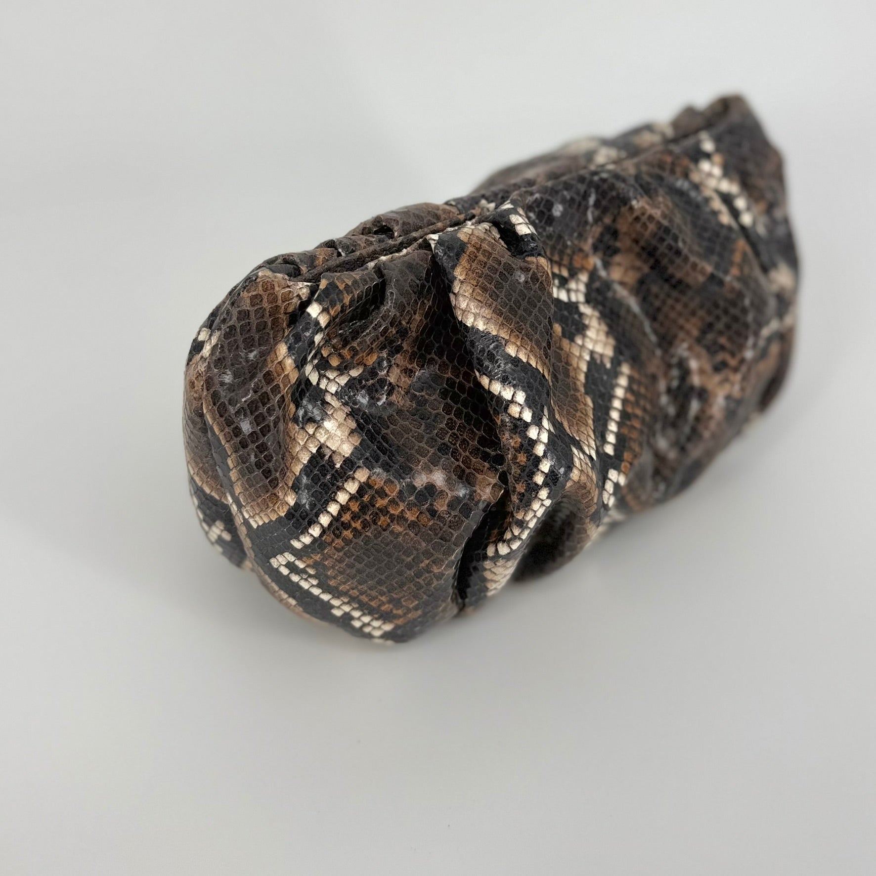 Detailed picture of small clutch bag with a brown and black snakeskin pattern, photographed against a neutral light gray background.