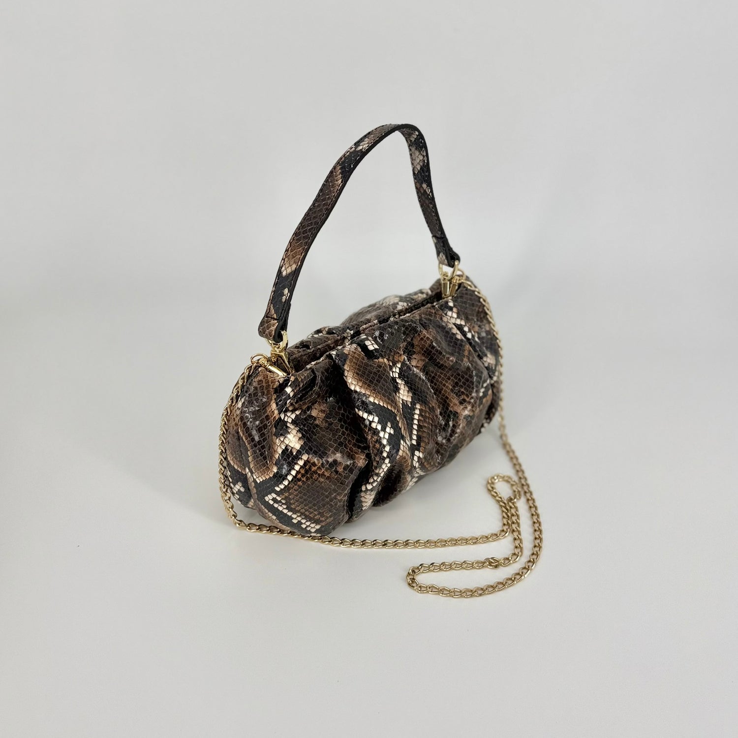 A small clutch bag with a brown and black snakeskin pattern, shown with the short and long strap, photographed against a neutral light gray background. 