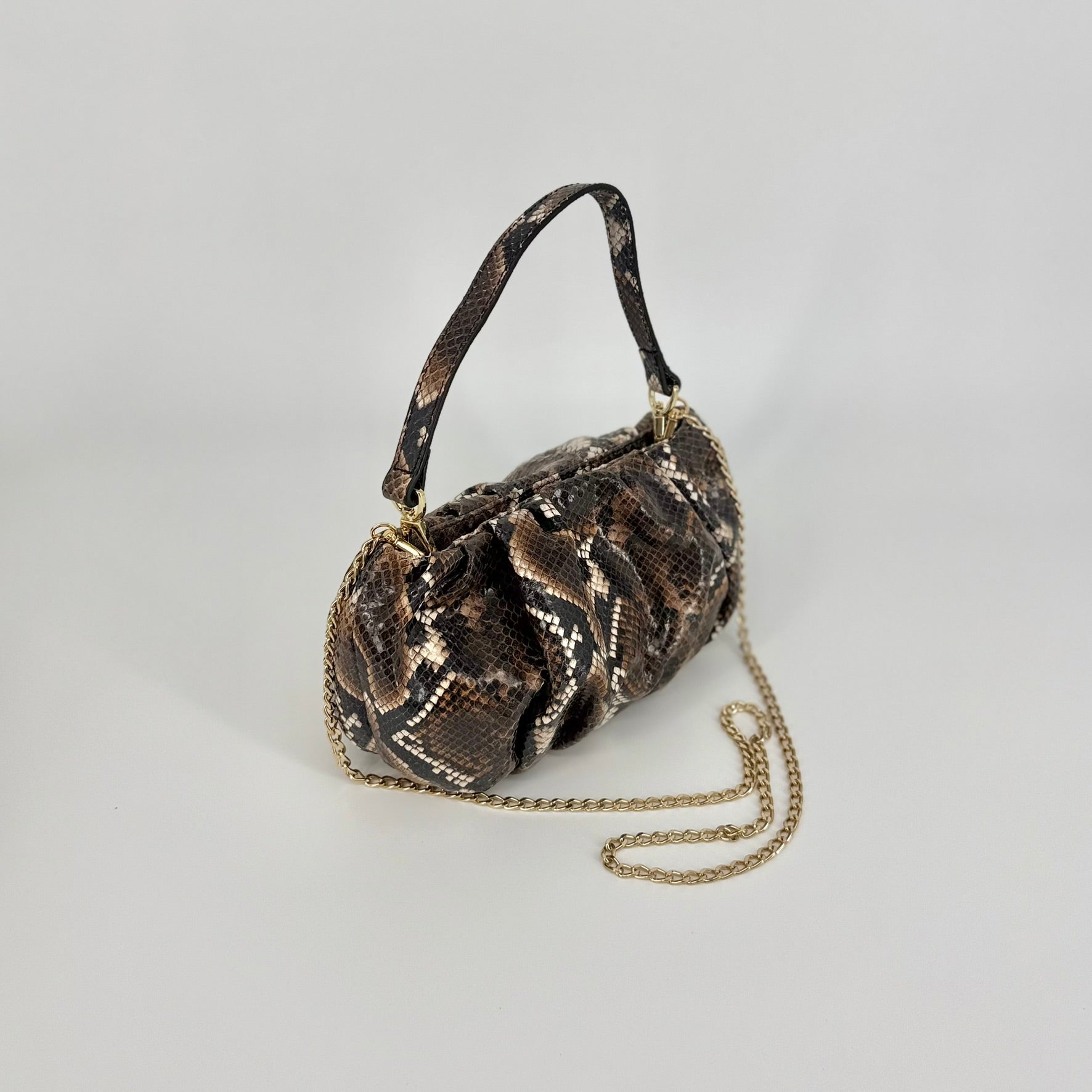 A small clutch bag with a brown and black snakeskin pattern, shown with the short and long strap, photographed against a neutral light gray background. 