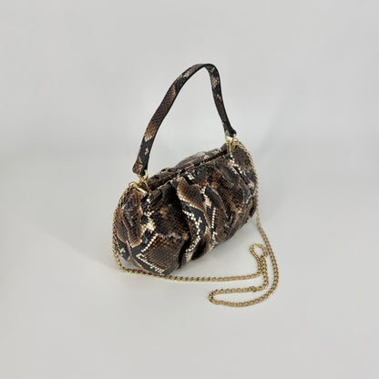 A small clutch bag with a brown and black snakeskin pattern, shown with the short and long strap, photographed against a neutral light gray background. 