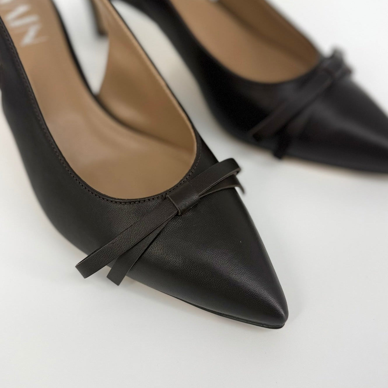 A pair of dark brown pointed-toe slingback pumps with a small bow detail on the toe, shown on a clean white background.