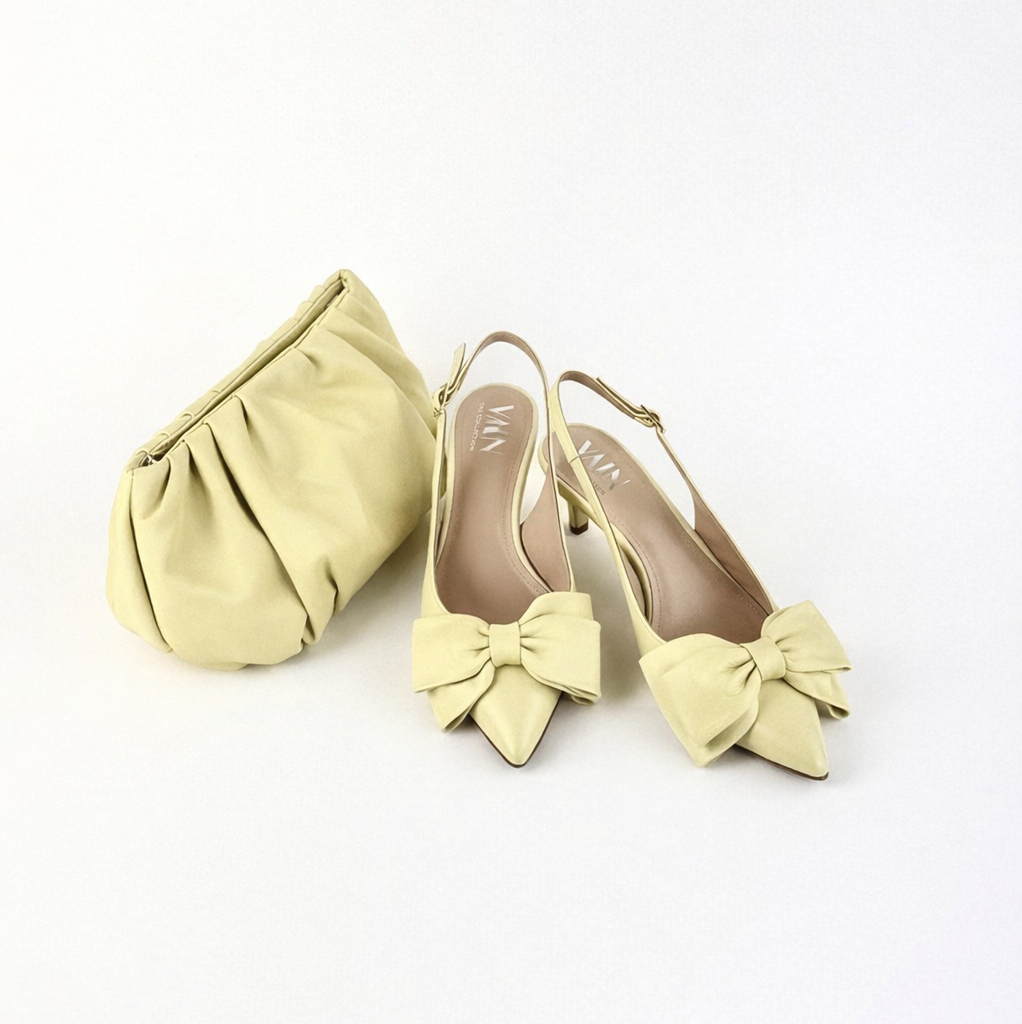 Pair of light yellow high heels with bow details and a matching clutch on a white background