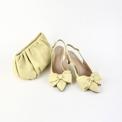 Pair of light yellow high heels with bow details and a matching clutch on a white background
