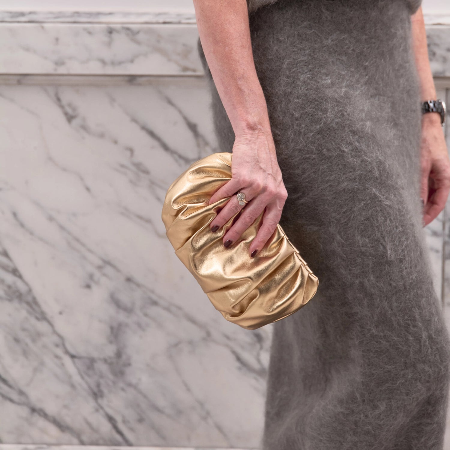 Person holding a gold clutch against a marble wall