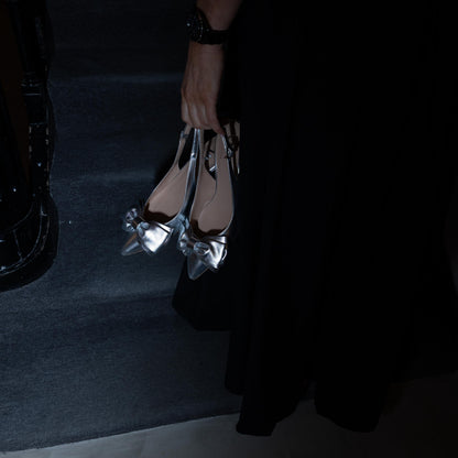 Person holding a set of silver low heels kitten sling backs in a dark setting