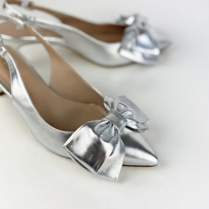 Silver pointed-toe sling back kitten heels with bow details on a light background
